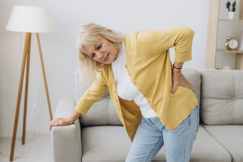 Senior woman bent over with back pain in living room, wishing for neck and back pain relief.